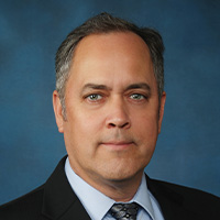 Man in black suit with a blue shirt and tie. 