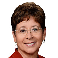A woman with short, dark hair and glasses smiles at the camera. 