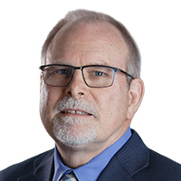 A man wearing glasses and a suit and tie smiles at the camera. 