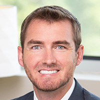 A  smiling man wearing a white collared shirt and suit jacket. 
