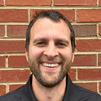 Man in black polo shirt smiles at the camera. 