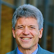 man in blue shirt and jacket smiles at the camera