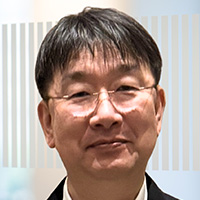 Man with short black hair wearing a black suit and glasses. 