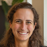 Woman with curly brown hair smiles at the camera.