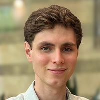 Man with wavy brown hair wearing a light green shirt smiles at the camera. 