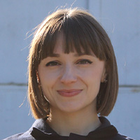 A woman with short dark hair wearing a dark jumpsuit smiles at the camera. 