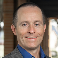 Man in blue shirt and tan jacket.