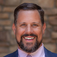 Man wears suit and tie and smiles at the camera. 