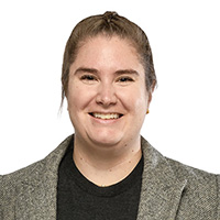 A woman in blue jeans, a black shirt, and jacket smiles at the camera. 