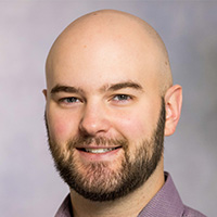 Man with no hair and brown beard smiles at the camera. 