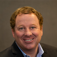 Man in jacket and tie smiles at the camera.