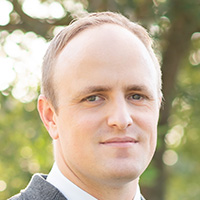 Man in suit and tie smiles at the camera.