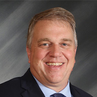 Man wears suit and tie and smiles at the camera. 