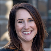 Woman with dark brown hair wearing a navy jacket and blouse smiles at the camera. 