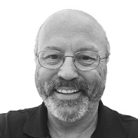 Man with glasses wearing a dark polo shirt smiles at the camera. 