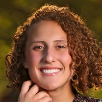 A woman with curly red hair in a polka dot shirt smiles at the camera. 