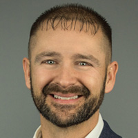 Man in jacket and shirt smiles at the camera.