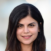 Woman with dark brown hair and wearing a white blouse smiles at the camera. 