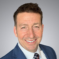 Man in jacket and tie smiles at the camera.