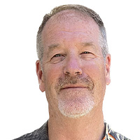 Man in Hawaiian shirt smiles at camera.