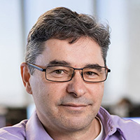 Man wearing glasses and a pink shirt smiles at the camera.