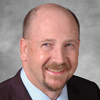 Man in jacket and tie smiles at the camera.