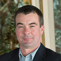 Man wearing shirt and jacket smiles at the camera.