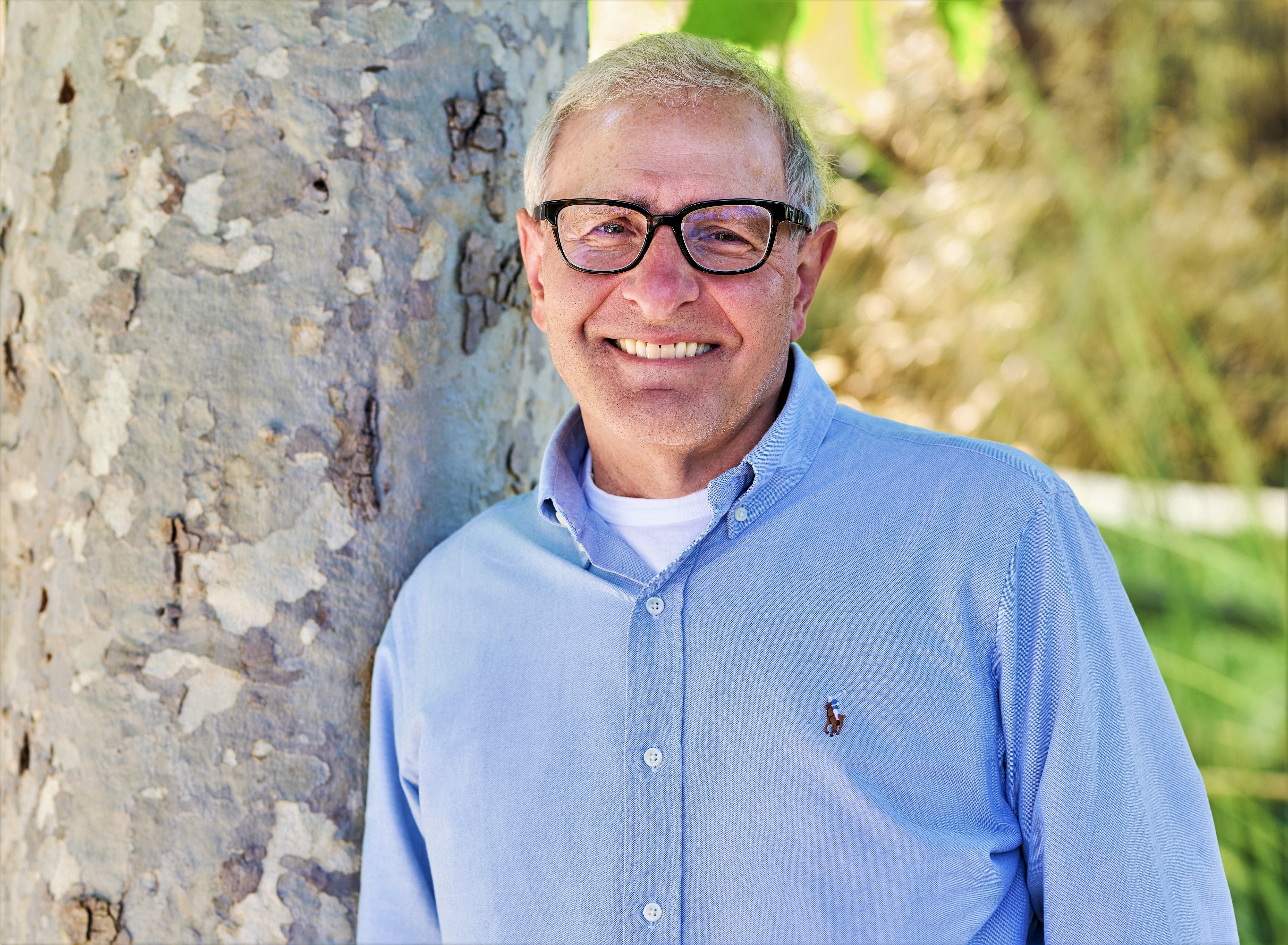Man in blue shirt stands next to a tree