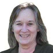 A woman with shoulder-length hair, wearing a pink shirt and a cardigan, smiles.