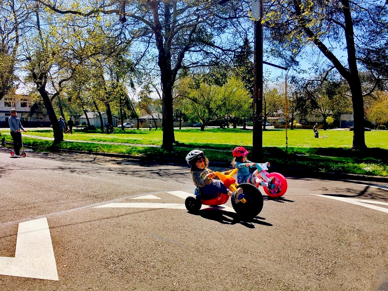 kids ride big wheels on a street