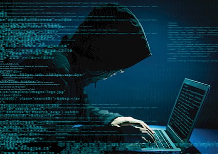 man in hooded sweatshirt hunched over a computer keyboard