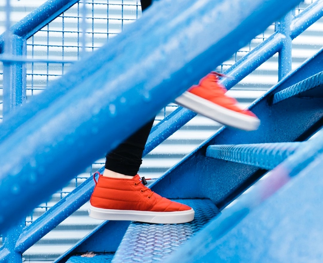 woman in orange tennis shoes and black pants walking up blue steps