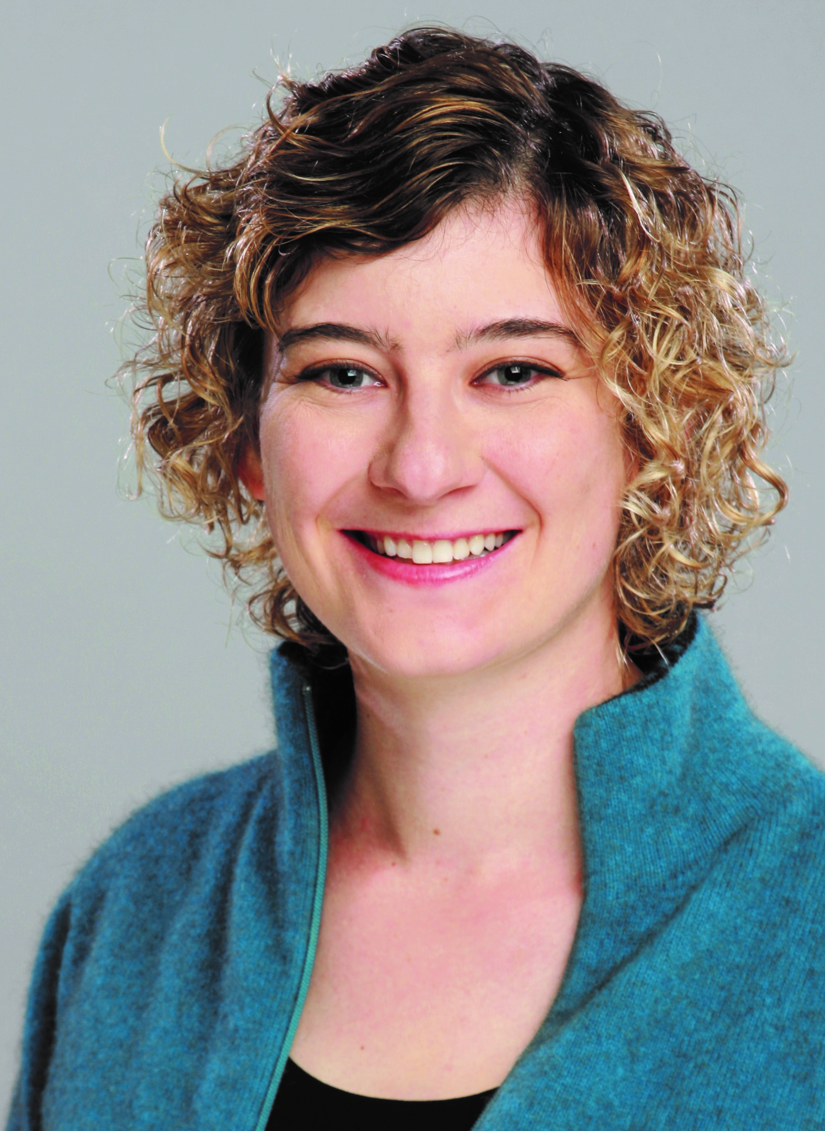 white woman with short curly hair wearing a turquoise jacket