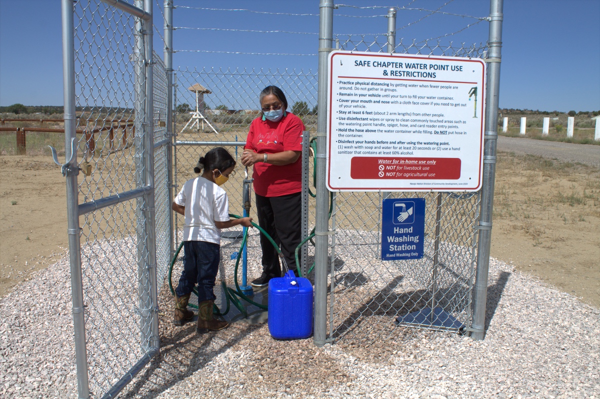 a woman and child fill a container with a hose