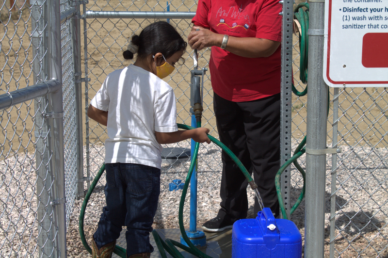 a child and women fill a container from a hose