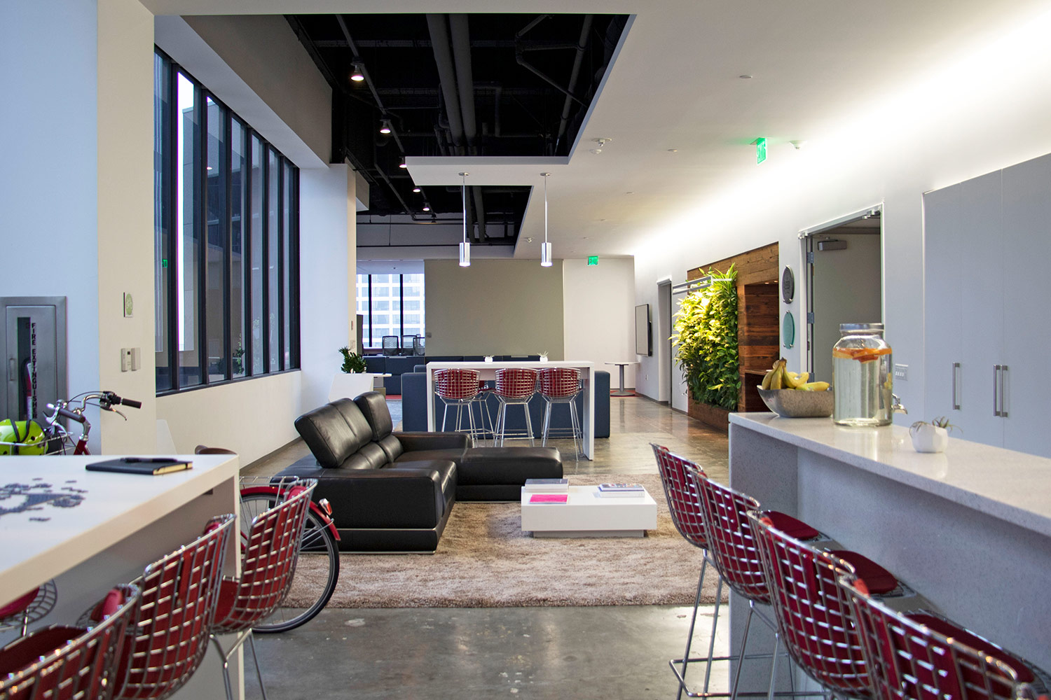 an office is set up as a combination living room and coffee shop with stools, tall tables, and a leather sofa