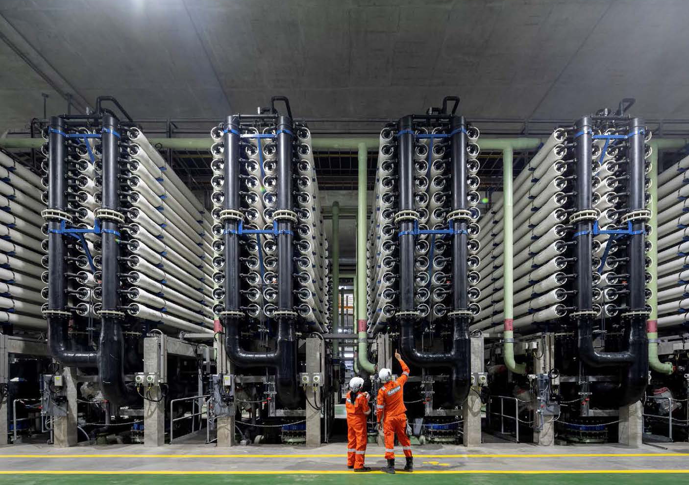 two orange jump-suited workers look up at three story high mechanical equipment