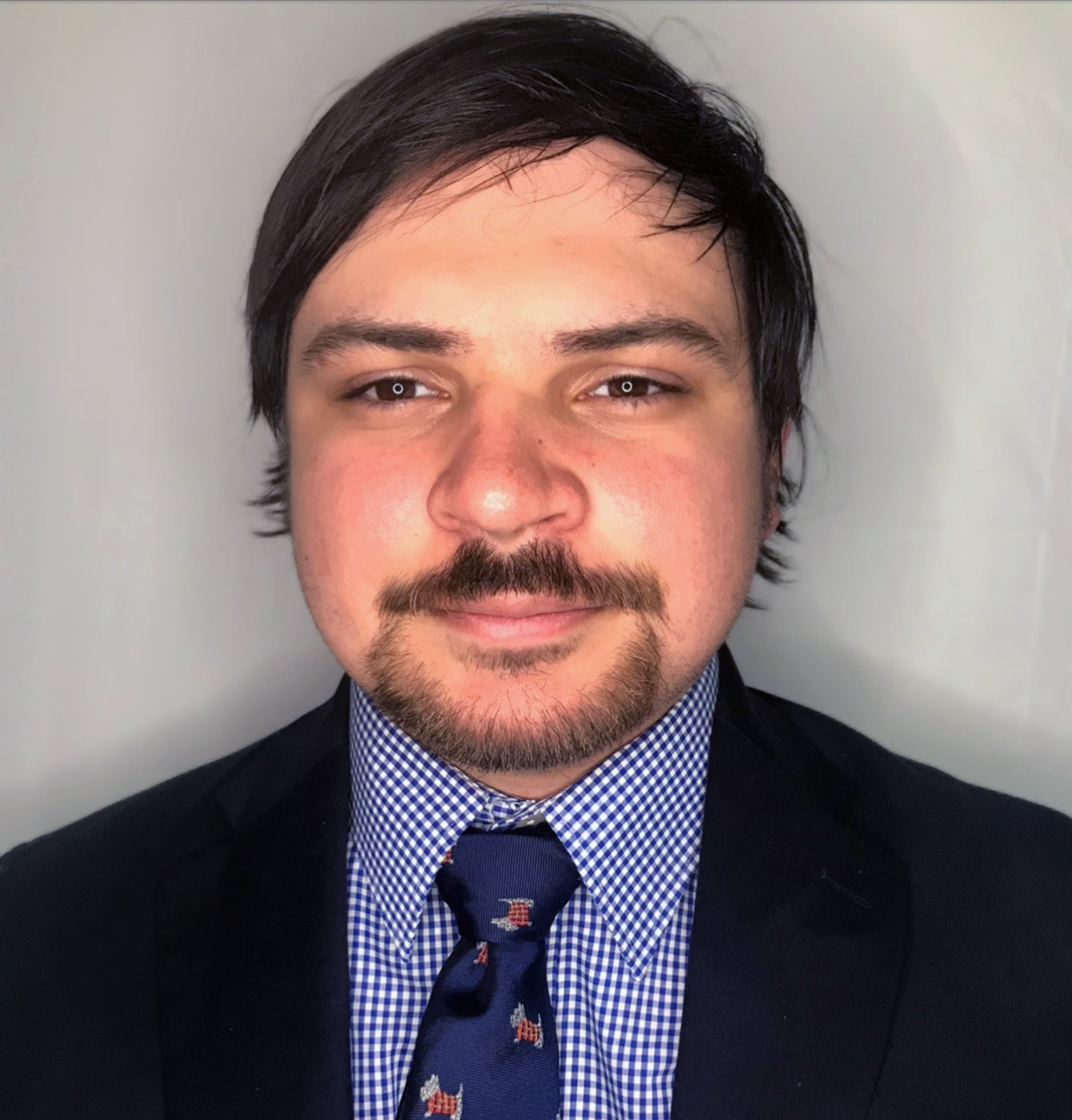 headshot of young man wearing a blue shirt and tie and black suit