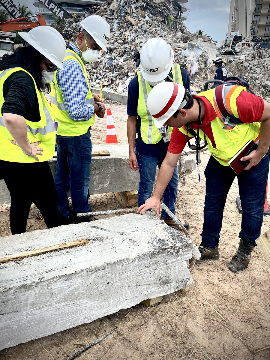 people in masks and yellow vests look at a concrete column laying on the ground