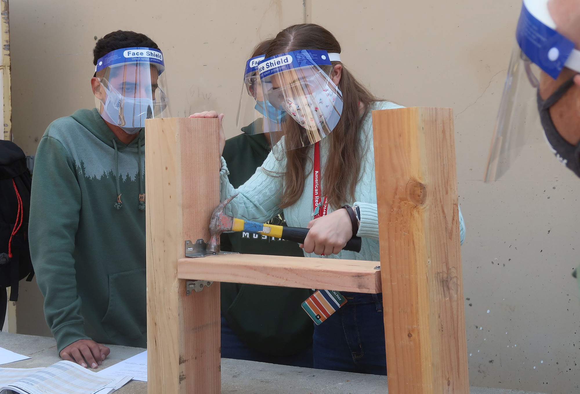female student testing a timber connection embedded in wood. two male students and the instructor are observing.