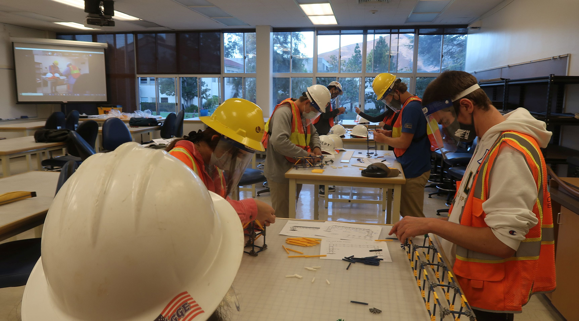 students in safety vests, face shields, and hard hats take part in a design, bid, build exercise where they assemble structures