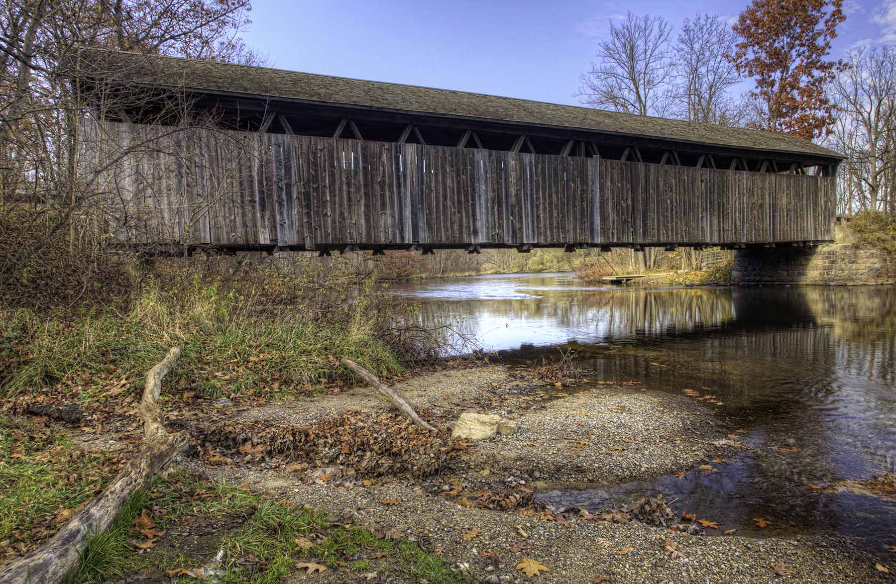 one lane wooden bridge built in 1869 spanning a small body of water. it has a gabled roof and wood siding