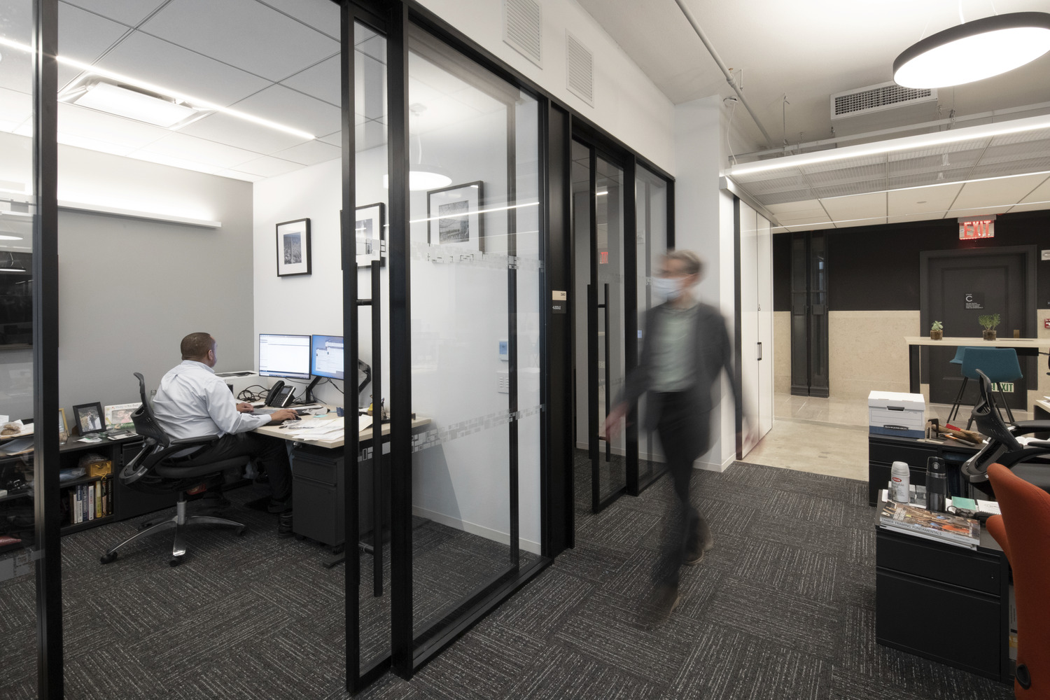 two workers in an office, one walking in a hallway and one sitting at a desk