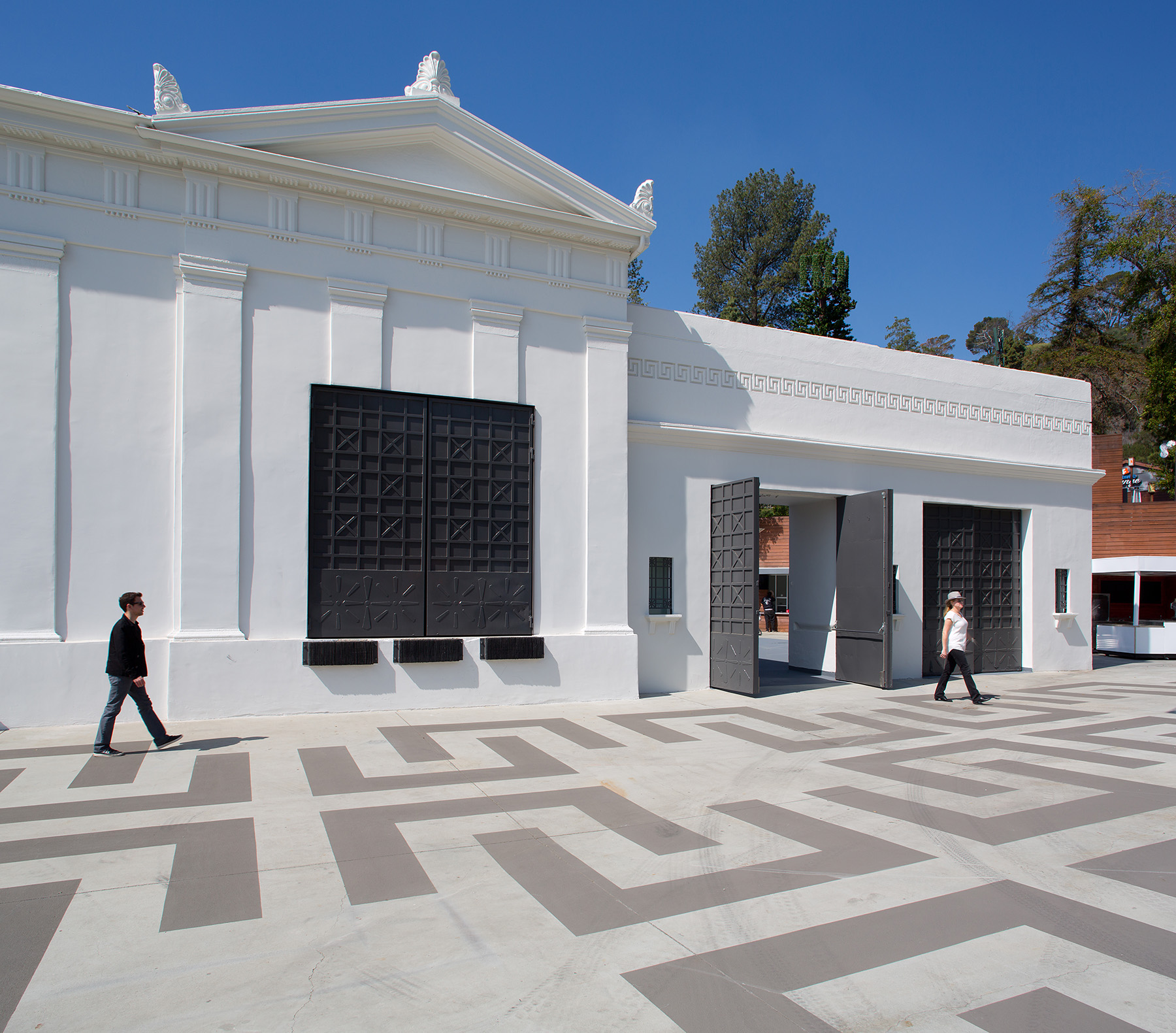 man and woman walking on patterned pavement in front of a white marble building