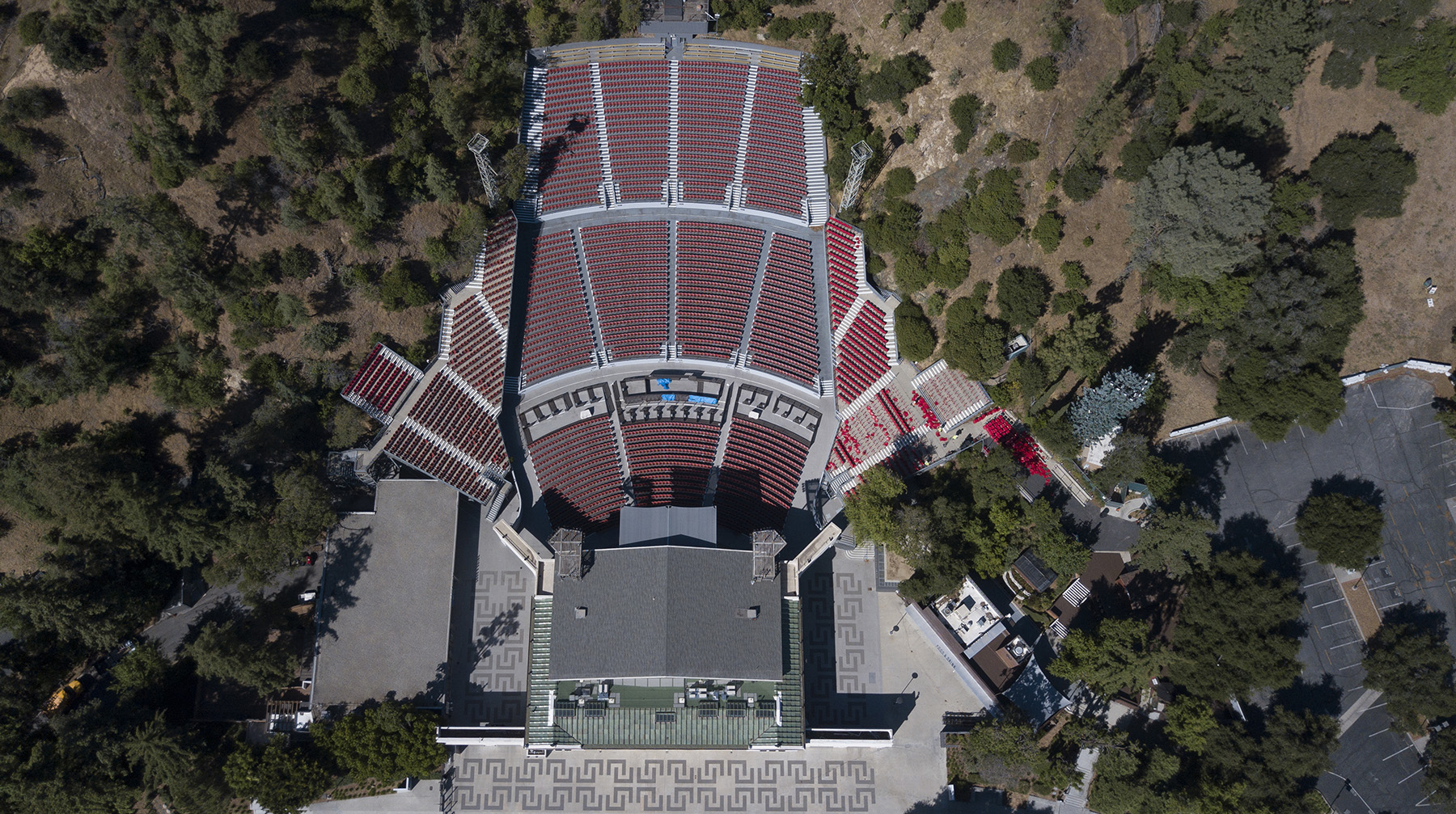 aerial photo of outdoor theatre showing entrance, seating, patterned concrete walkway, and surrounding trees and hills