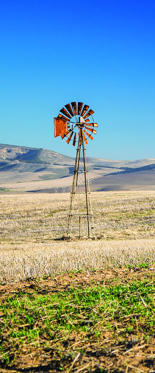 windmill in a dry, brown field. a clear blue sky is overhead and there are hills in the background