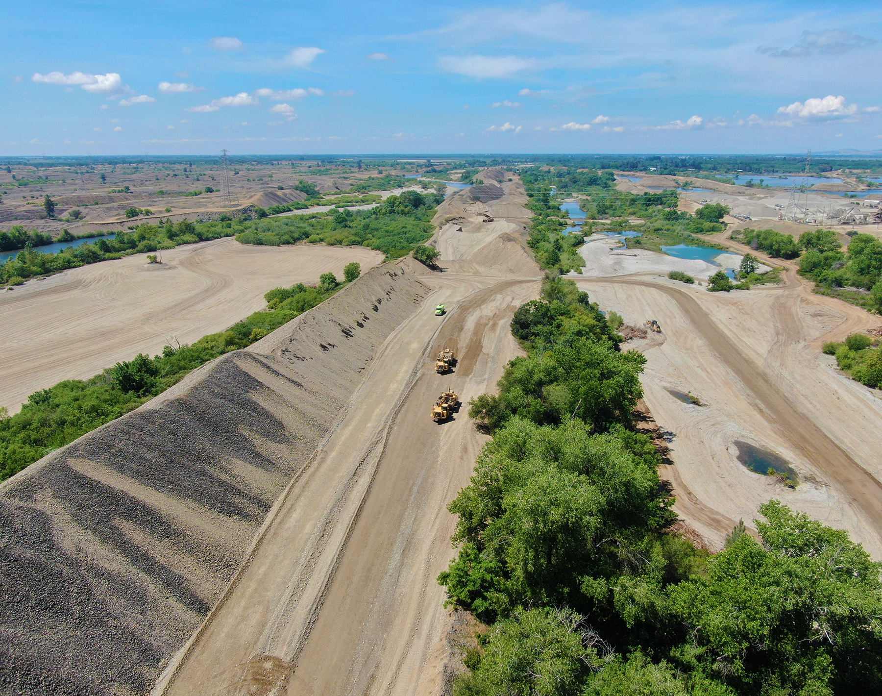 photograph showing land punctuated by meandering waterways, construction equipment, and trees