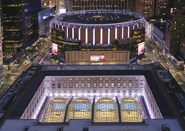 cityscape showing skyscrapers, midrise buildings, and low-rise buildings, a circular building that has signs on it, and a rectangular building with a sunken section that is topped by glass.