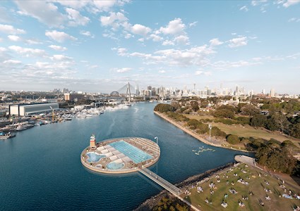 image shows a walkway leading to a round concrete structure. this structure has three pools on it. the structure is surrounded by water and land masses.