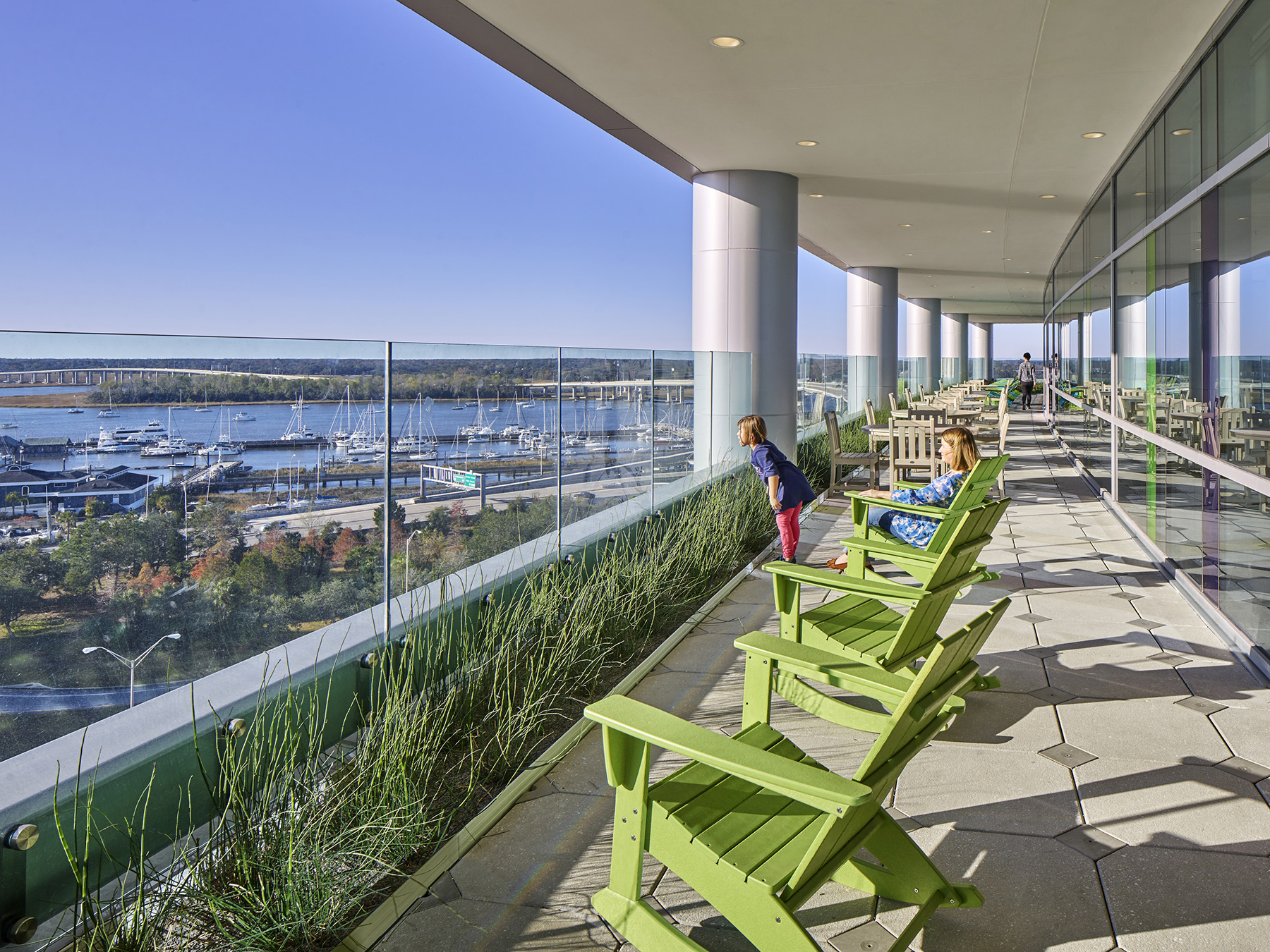 photo showing an observation deck overlooking a body of water. There are boats in the water, and there is a girl and woman looking out at the water.